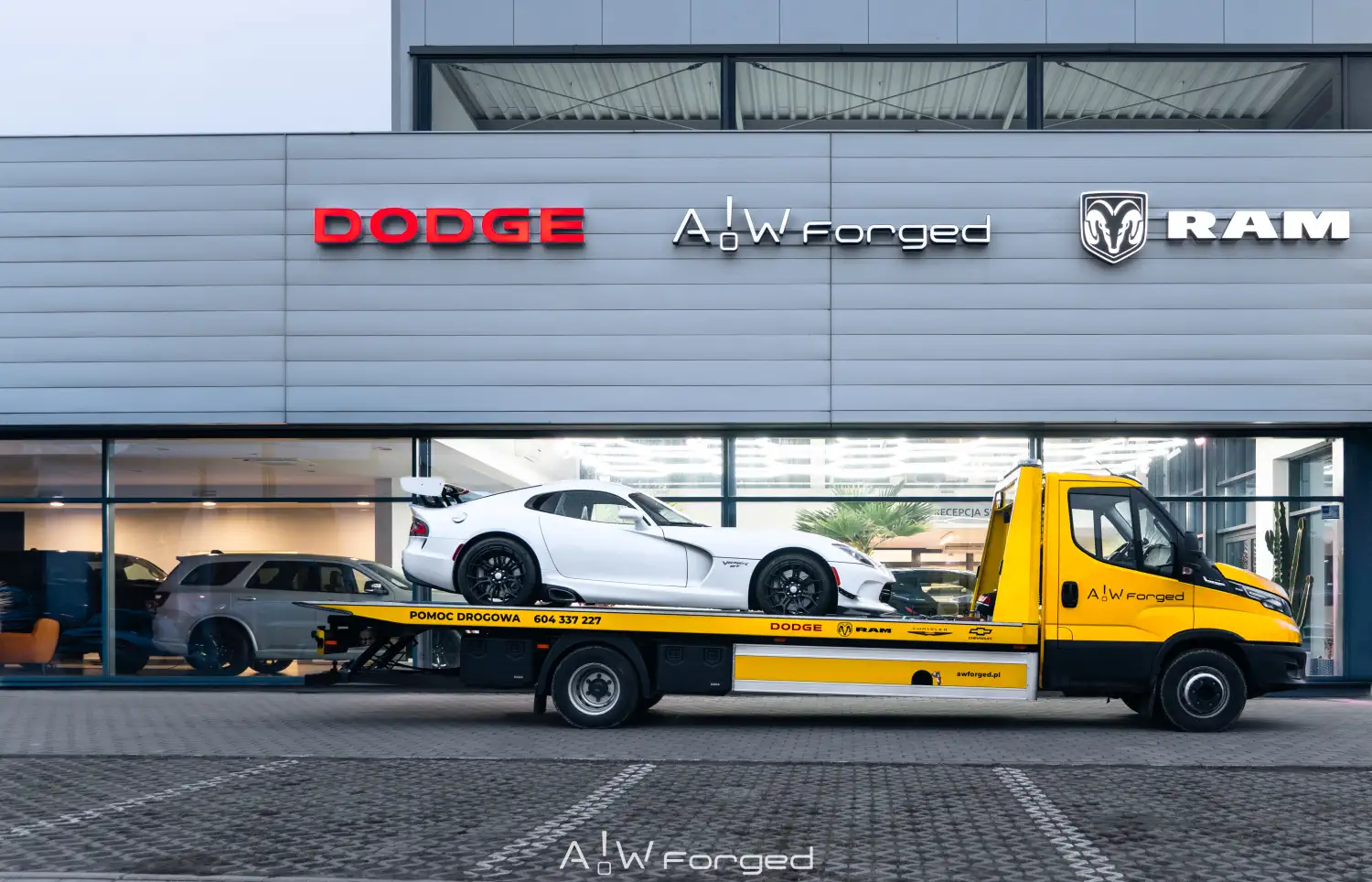 Żółta laweta Pomoc Drogowa A!W forged z autem Dodge Viper Time Attack II na pace, na tle serwisu A!W Forged