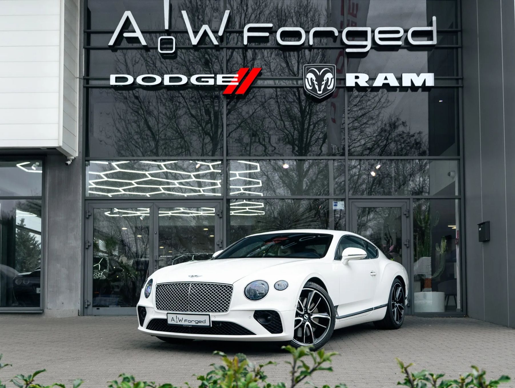 Biały Bentley Continental GT przed salonem samochodowym A&W Forged.